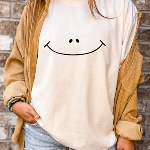 May include: A white long-sleeved t-shirt with a black smiley face graphic.