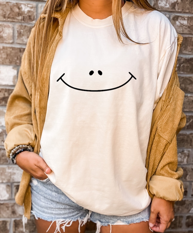 May include: A white long-sleeved t-shirt with a black smiley face graphic.