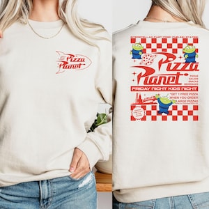 Peut inclure: Un sweat-shirt cr&egrave;me avec un motif rouge et blanc du logo Pizza Planet et le texte "Pizza Planet" et "Friday Night Kids Nicht". Le motif comprend &eacute;galement un motif &agrave; carreaux et des personnages d'extraterrestres de dessin anim&eacute;.