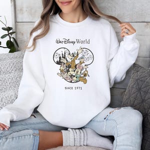 Puede incluir: Sudadera blanca con un gr&aacute;fico de Mickey Mouse y sus amigos frente al Castillo de Cenicienta. El texto "Walt Disney World" y "Since 1971" est&aacute; impreso en la sudadera.