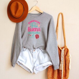 May include: Gray sweatshirt with the text "Borracha Pero Buena Muchacha" in pink and blue with a red rose graphic.