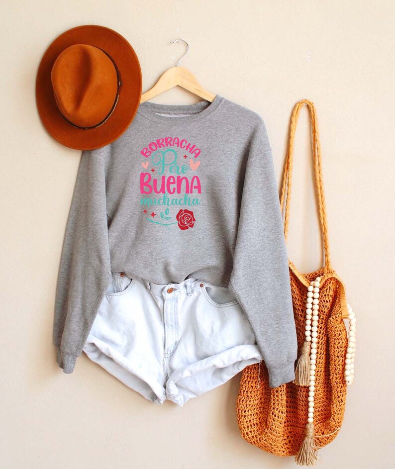 May include: Gray sweatshirt with the text "Borracha Pero Buena Muchacha" in pink and blue with a red rose graphic.