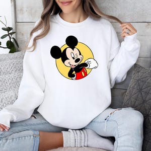 May include: White sweatshirt with a yellow circle and a cartoon image of Mickey Mouse in a red and black outfit. Mickey Mouse is winking and giving a thumbs up.