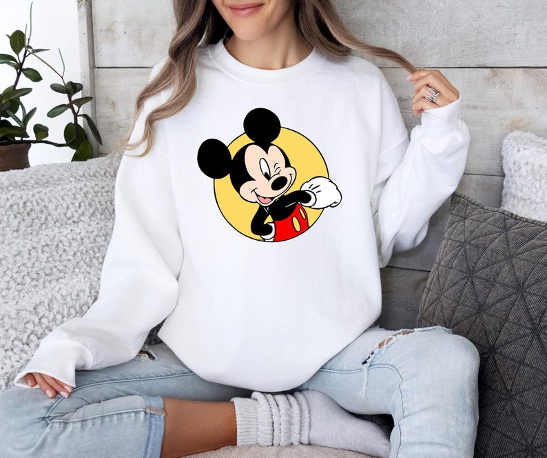 May include: White sweatshirt with a yellow circle and a cartoon image of Mickey Mouse in a red and black outfit. Mickey Mouse is winking and giving a thumbs up.