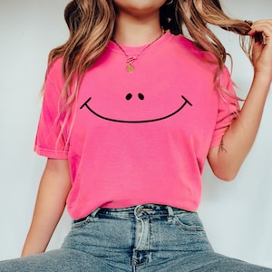 May include: A pink t-shirt with a black smiley face graphic. The shirt is made of a soft, comfortable material and has a relaxed fit.