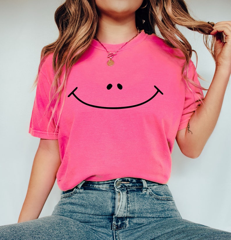May include: A pink t-shirt with a black smiley face graphic. The shirt is made of a soft, comfortable material and has a relaxed fit.