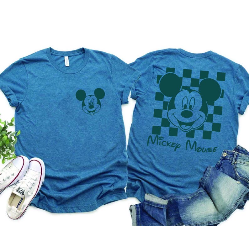 Pu&ograve; includere: Una maglietta blu con un'immagine verde di Topolino sul davanti e un'immagine verde di Topolino pi&ugrave; grande con uno sfondo a scacchi sul retro. Il testo "Mickey Mouse" &egrave; stampato sotto l'immagine sul retro.