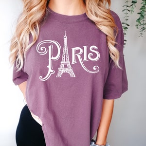 May include: A purple t-shirt with a white graphic of the Eiffel Tower and the word "PARIS" in a stylized font.