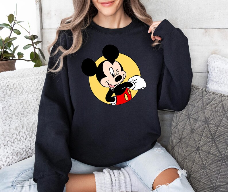 May include: Black sweatshirt with a yellow circle and a cartoon image of Mickey Mouse in a red and black outfit. Mickey Mouse is winking and giving a thumbs up.