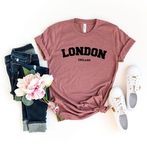 May include: A mauve t-shirt with the text "LONDON ENGLAND" in black block letters.