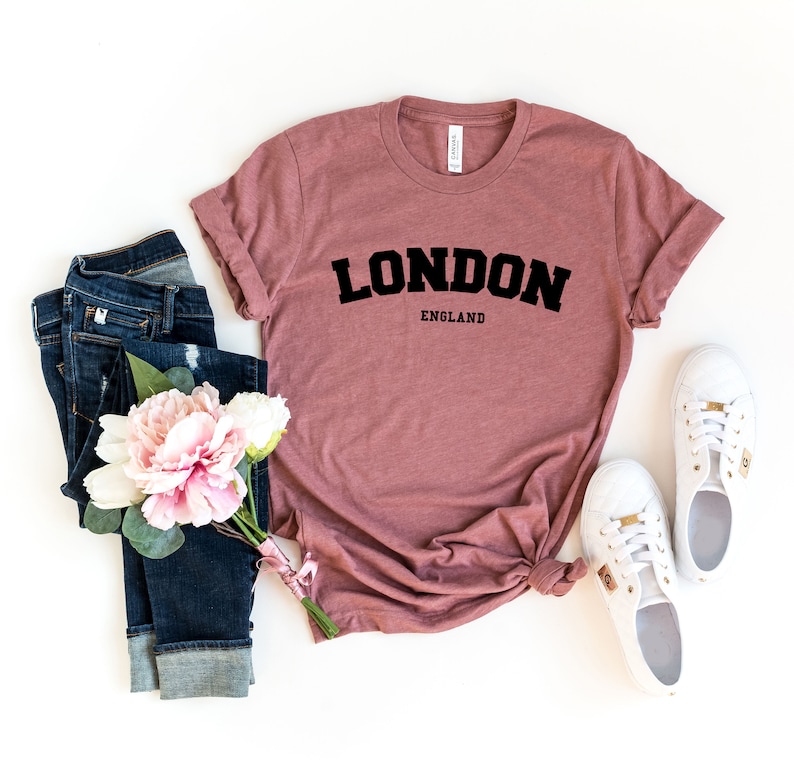 May include: A mauve t-shirt with the text "LONDON ENGLAND" in black block letters.