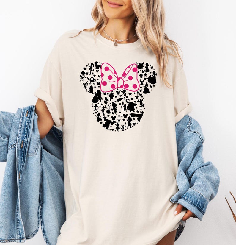 May include: A white t-shirt with a black silhouette of Mickey Mouse's ears filled with Disney characters. The bow on top of the ears is pink with white polka dots.