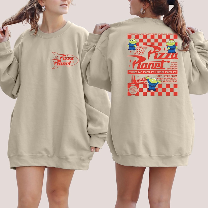 Peut inclure: Un sweat-shirt beige avec un graphique de fus&eacute;e et le texte "Pizza Planet" sur le devant. Le dos du sweat-shirt pr&eacute;sente un motif &agrave; carreaux avec le texte "Pizza Planet" et un personnage d'alien de dessin anim&eacute;.