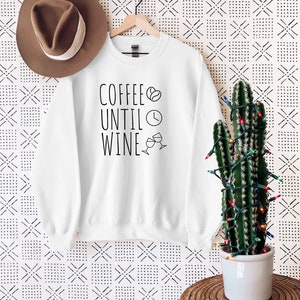 May include: White sweatshirt with the text "Coffee Until Wine" in black lettering. A coffee bean, clock, and wine glass icons are included in the design.