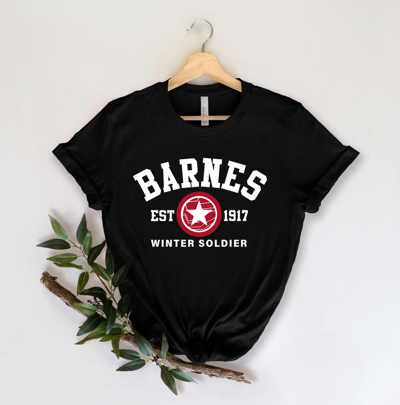 May include: Black t-shirt with the word "BARNES" in white block letters above "EST 1917" and "WINTER SOLDIER". A red and white star emblem is centered below "EST 1917". The shirt is hanging on a wooden hanger against a white background.