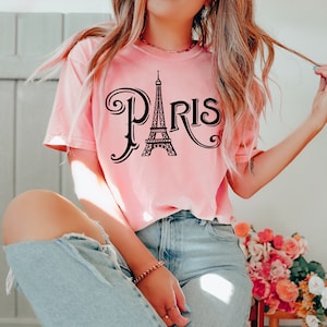 May include: A pink t-shirt with a black graphic of the Eiffel Tower and the word "Paris" in a stylized font.