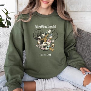 Puede incluir: Una sudadera verde con un gr&aacute;fico blanco de Mickey Mouse y sus amigos frente al castillo de Walt Disney World. El texto "Walt Disney World" y "Since 1971" est&aacute; impreso en la sudadera.