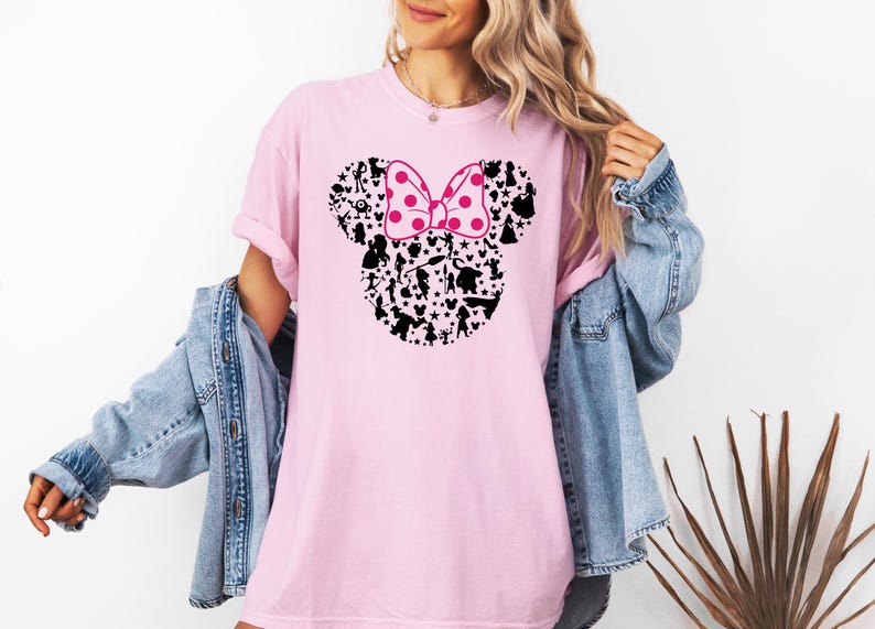 May include: A pink t-shirt with a black silhouette of Mickey Mouse's head made up of various Disney characters. The bow is pink with white polka dots.