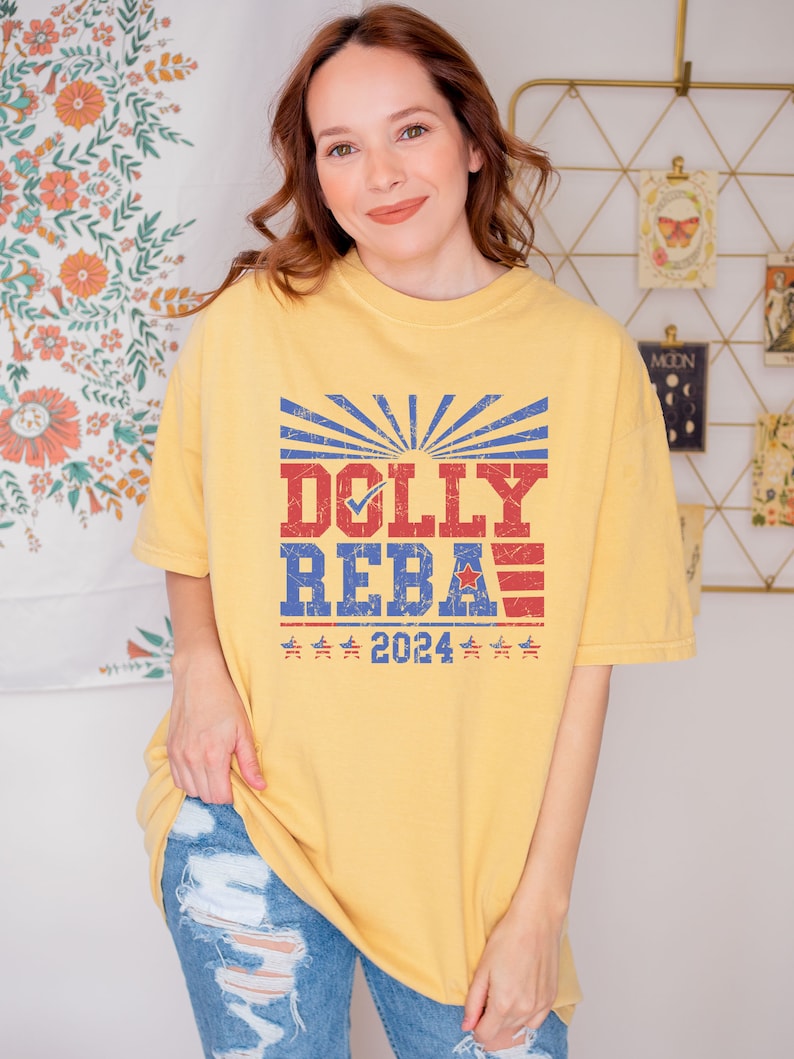 May include: A yellow t-shirt with a vintage-style graphic featuring the text "DOLLY REBA" with a checkmark next to "DOLLY" and a red, white, and blue American flag design. The text "2024" is below the graphic.