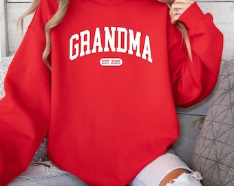 Może przedstawiać: Czerwony sweter z białym napisem "Grandma Est. 2025".