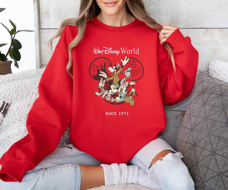 Puede incluir: Sudadera roja con un gr&aacute;fico blanco de Mickey Mouse y sus amigos frente a un espect&aacute;culo de fuegos artificiales. El texto "Walt Disney World" y "Since 1971" est&aacute;n impresos en la sudadera.