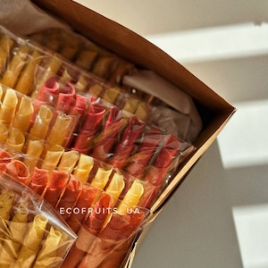 May include: A box filled with colorful fruit leather rolls. The rolls are packaged in clear plastic and arranged in rows. The box is labeled "ECOFRUITS UA".