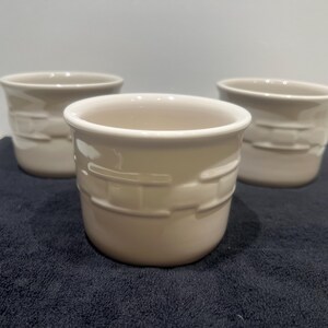 May include: Three beige ceramic pots with a textured, basket-weave design. The pots have a rounded shape and a smooth, off-white interior. They are arranged on a dark blue surface, creating a neutral and versatile aesthetic. Ideal for small plants or decorative storage.