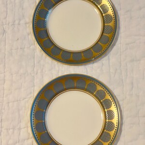 May include: Two small, white ceramic plates with a blue and gold geometric pattern around the rim.