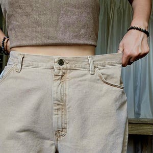 以下が含まれることがあります： ベージュ色のハイウエストジーンズ。ボタン留めとクラシックな5ポケットデザイン。ジーンズは、お揃いのベージュのクロップトップと組み合わせています。全体的にニュートラルな色合いでカジュアルなスタイルです。