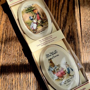May include: A boxed set of two oval-shaped soaps featuring illustrations from Beatrix Potter's stories. The top soap depicts Jemima Puddle-Duck, while the bottom soap shows Peter Rabbit with his family. The packaging reads "pictorial soap london."