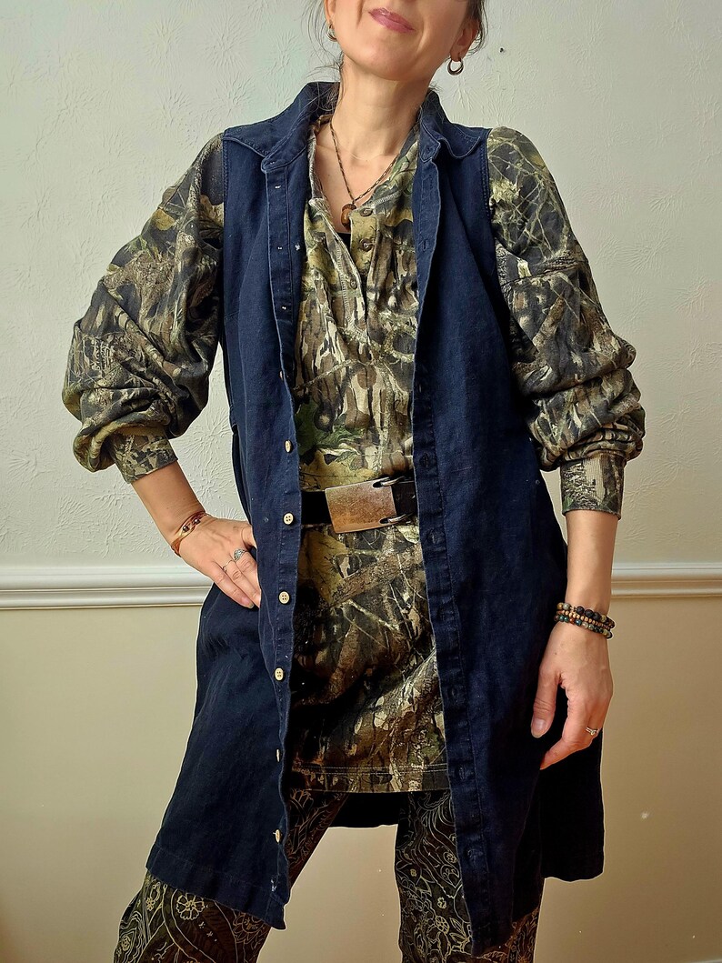 K&ouml;nnte beinhalten: Eine dunkelblaue Jeansweste &uuml;ber einem Hemd und einer Hose mit Camouflage-Muster. Das lang&auml;rmlige Hemd hat eine Knopfleiste und einen Kragen. Die Hose hat ein dekoratives Muster. Ein brauner G&uuml;rtel mit Metallschnalle wird in der Taille getragen.