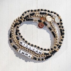 May include: Four beaded bracelets. Two bracelets are gold and black, and two are gold. The bracelets have the names "WILLIAM" and "EMMA" spelled out in white letter beads. Gold sunflower charms are also included.