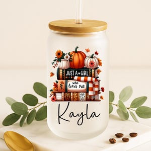 May include: A frosted glass tumbler with a bamboo lid and straw. The tumbler features a fall-themed design with pumpkins, flowers, and the text "JUST A GIRL who loves Fall" and the name "Kayla".