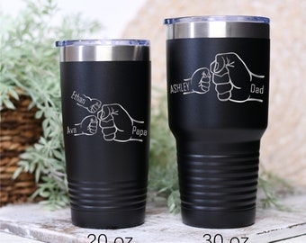 May include: Two black stainless steel tumblers with a fist bump design and personalized names. The smaller tumbler is 20 oz and the larger tumbler is 30 oz. The names on the smaller tumbler are Ava, Ethan, and Papa. The names on the larger tumbler are Ashley and Dad.