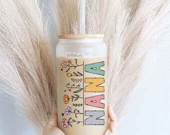 May include: A frosted glass tumbler with a bamboo lid and a straw. The tumbler has a floral design and the word "NANA" written in colorful letters.