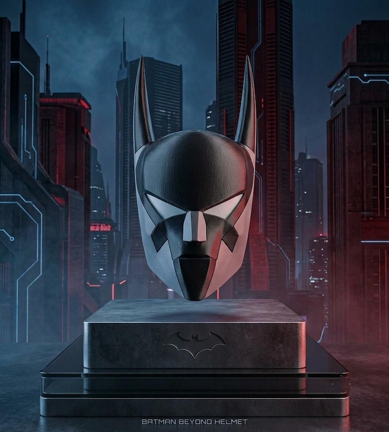 K&ouml;nnte beinhalten: Ein schwarz-wei&szlig;er Batman Beyond Helm mit spitzen Ohren und einem schlanken, kantigen Design. Der Helm ist auf einem rechteckigen Sockel mit einem Fledermaus-Emblem ausgestellt, wobei der Text BATMAN BEYOND HELMET unten aufgedruckt ist.