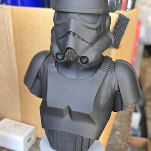 May include: Black and grey 3D printed bust of a Star Wars Stormtrooper. The bust is detailed with a helmet, chest plate, and shoulder pads.