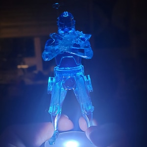 May include: A blue translucent plastic action figure of a Star Wars character standing on a round light-up base.