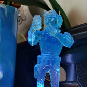 May include: A translucent blue action figure of a character from the Star Wars universe. The figure is holding a blaster in one hand and has a helmet on its head.