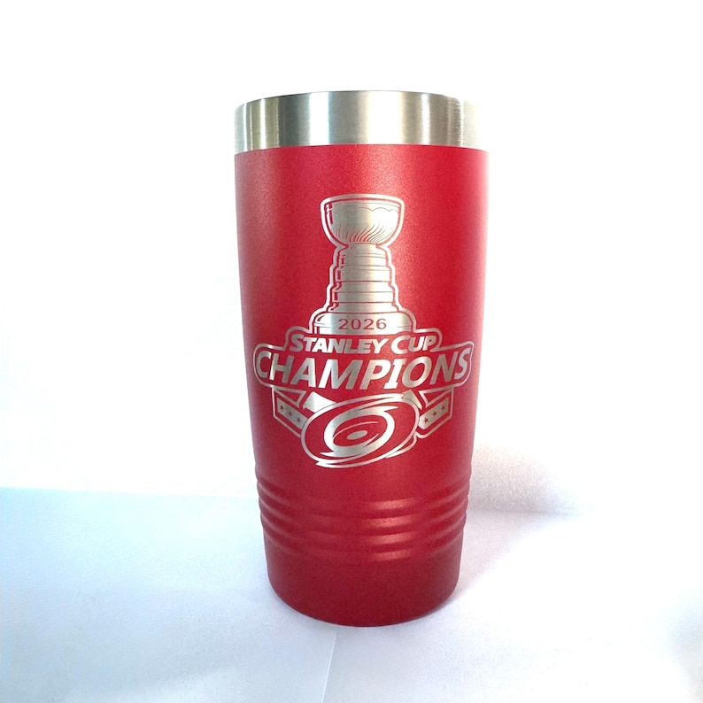 K&ouml;nnte beinhalten: Ein roter Edelstahlbecher mit silbernem Rand und einer lasergravierten Grafik, die den Stanley Cup, den Text 2026 STANLEY CUP CHAMPIONS und ein hurrikanartiges Logo in der Mitte des isolierten Getr&auml;nkebeh&auml;lters zeigt.