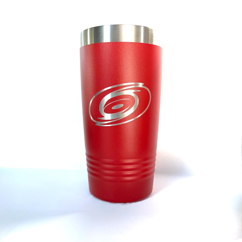 K&ouml;nnte beinhalten: Ein roter Edelstahlbecher mit silbernem Rand und einem lasergravierten Hurrikan-Logo auf der Vorderseite. Der zylindrische Beh&auml;lter verf&uuml;gt &uuml;ber drei horizontale Rillen nahe der Basis und eine glatte, matte Oberfl&auml;che an der Au&szlig;enseite.