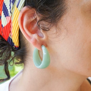 May include: A pair of large, light green hoop earrings. The earrings are made of a smooth, opaque material.