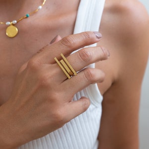 Könnte beinhalten: Goldener geometrischer Ring mit drei übereinanderliegenden rechteckigen Stäben.