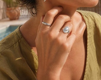 May include: A set of silver-toned jewelry including a curved earring, a thin textured band ring, a wider ring with a central oval accent, and a double-layered cuff bracelet. The jewelry features a polished metallic finish and smooth, organic shapes.