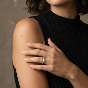 May include: A polished silver ring with an open, bypass-style design featuring two rounded, smooth ends that overlap slightly on the finger. The band has a reflective, metallic finish and a continuous, fluid shape that wraps around the finger.