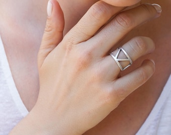 May include: A silver ring with a geometric design. The ring is wide and has a triangular pattern.
