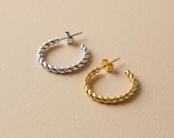 May include: Two hoop earrings featuring a twisted rope texture. One earring is finished in a bright silver tone, while the other is finished in a polished gold tone. Both earrings include a standard post and butterfly back closure mechanism.