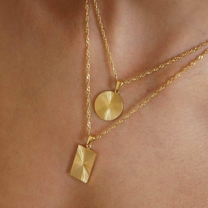 May include: Two gold necklaces with a round and a square pendant. Both pendants have a sunburst design.