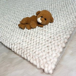 Puede incluir: Una alfombra blanca y esponjosa con un oso de peluche marr&oacute;n acostado encima.
