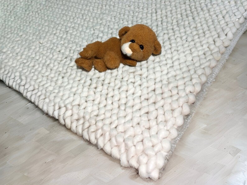 Puede incluir: Una alfombra blanca y esponjosa con un oso de peluche marr&oacute;n acostado encima.